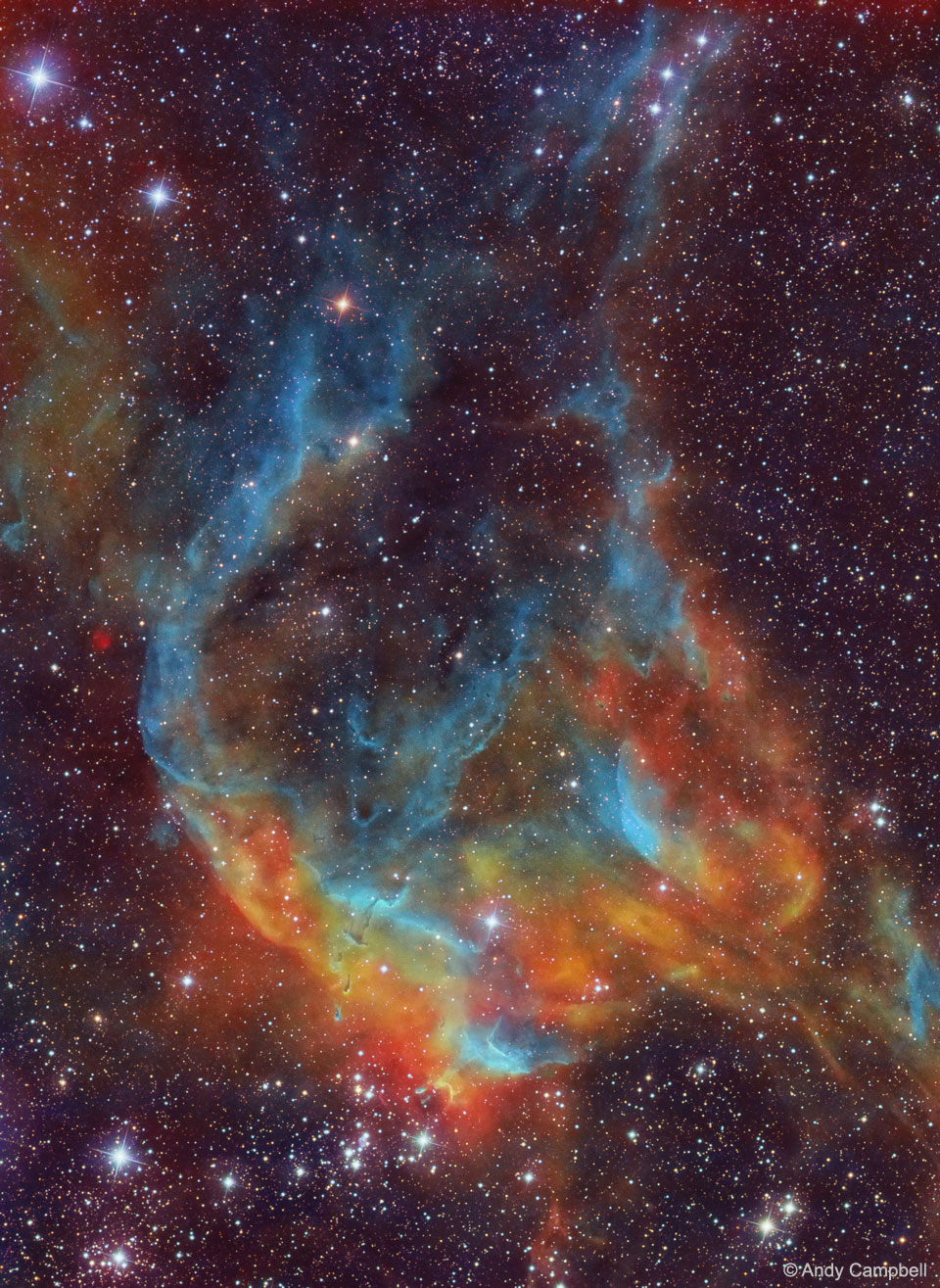 Im Bild leuchten Nebelranken in mattem Blau und hellerem Orangerot. Unten ist ein Sternhaufen, im Hintergrund sind viele kleine Sterne verteilt.