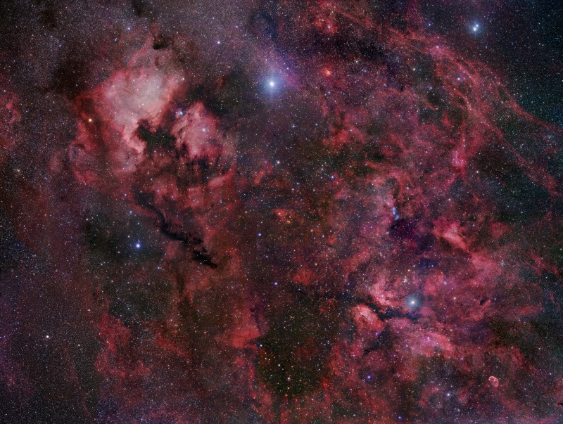 Das Bild ist voller rot leuchtender Nebel mit dunklen Nebeln und vielen Sternen dazwischen.