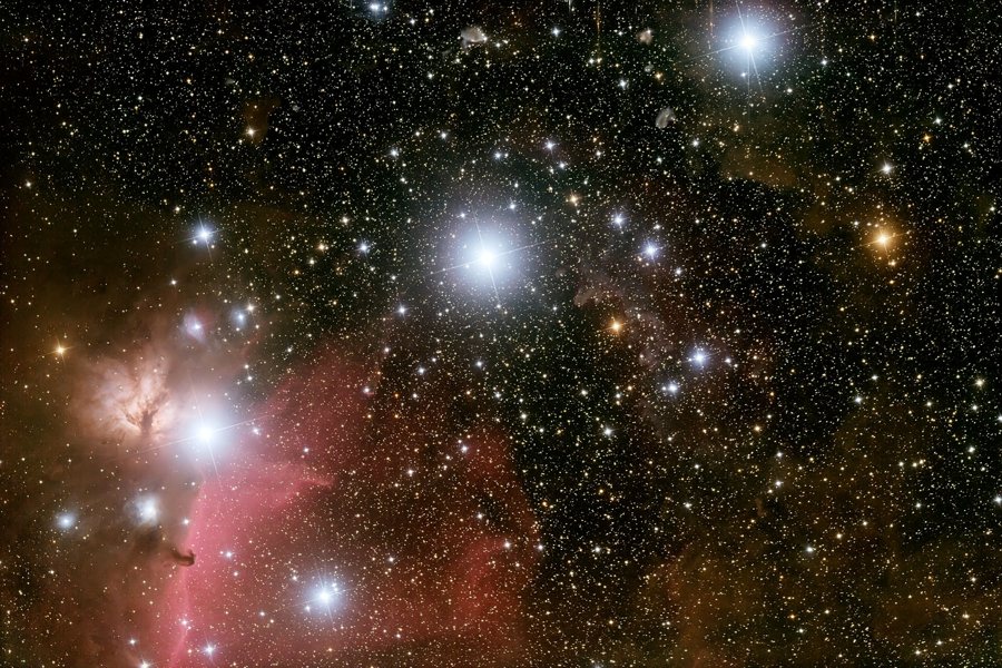 Das Sternenbild zeigt diagonal angeordnet die Gürtelsterne des Orion, links unten leuchtet der Flammennebel, und der Pferdekopfnebel zeichnet sich als Silhouette vor einem rötlichen Nebel ab.