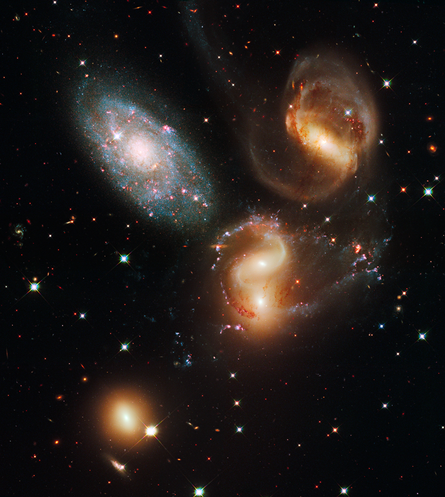 Im Bild sind fünf Galaxien verteilt, zwei davon kollidieren. Vier leuchten gelblich, die fünfte wirkt bäulich und besitzt mehr rötliche Sternbildungsregionen als andere.