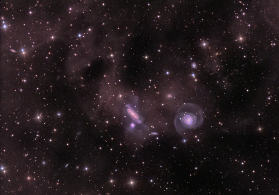Das Bild ist mit wenigen, aber hellen Sternen und schwachen Hintergrundnebeln gefüllt. In der Mitte leuchten zwei kleine verzerrte Spiralgalaxie sowie mehrere kleine Spiralen.