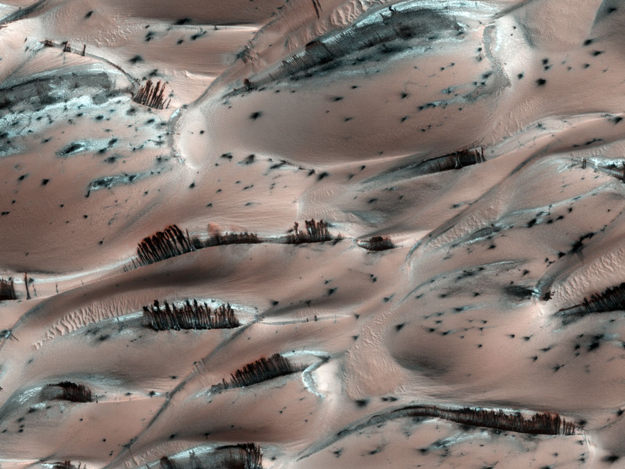 Braunrosa Dünen sind von dunklen Strukturen gesprenkelt, von den Hügelkuppen verlaufen schwarze Hangrutschungen abwärts.
