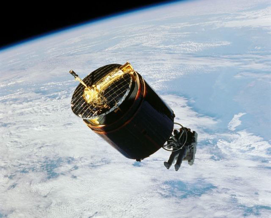 Ein Astronaut hält sich an einem Satelliten, im Hintergrund ist die Erde zu sehen, der Erdrand ist in der linken oberen Ecke.