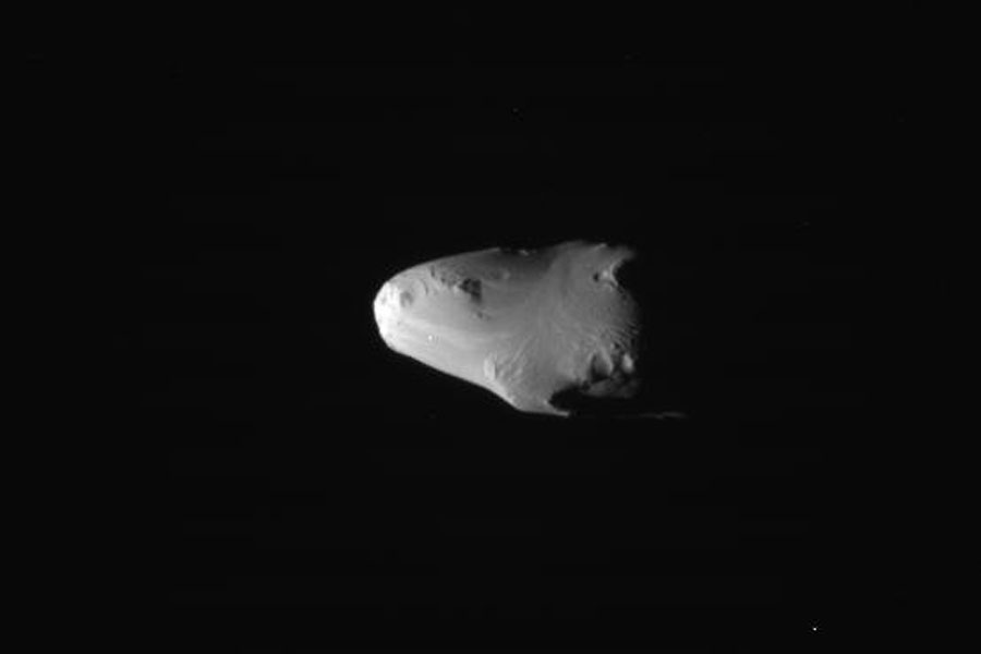Vor einem dunklen Hintergrund schwebt ein länglicher, vorne runder Körper ohne Krater, es ist der Saturnmond Calypso.