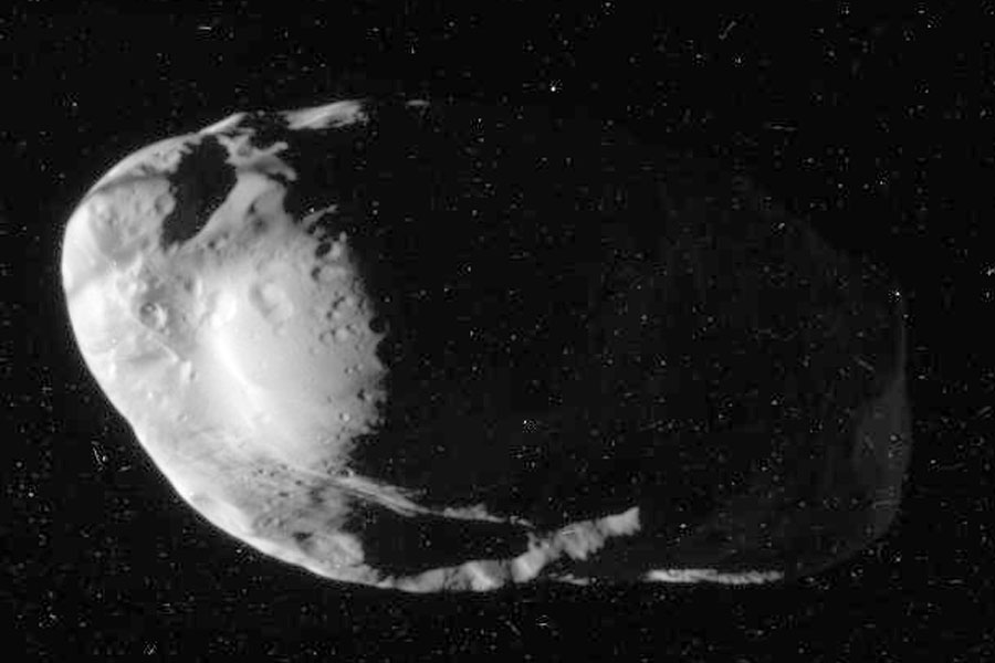 Ein Himmelskörper mit seltsamer Form und mehreren Kratern schwebt bildfüllend im Raum, er ist von links beleuchtet, die rechte Seite ist kaum erkenbar.