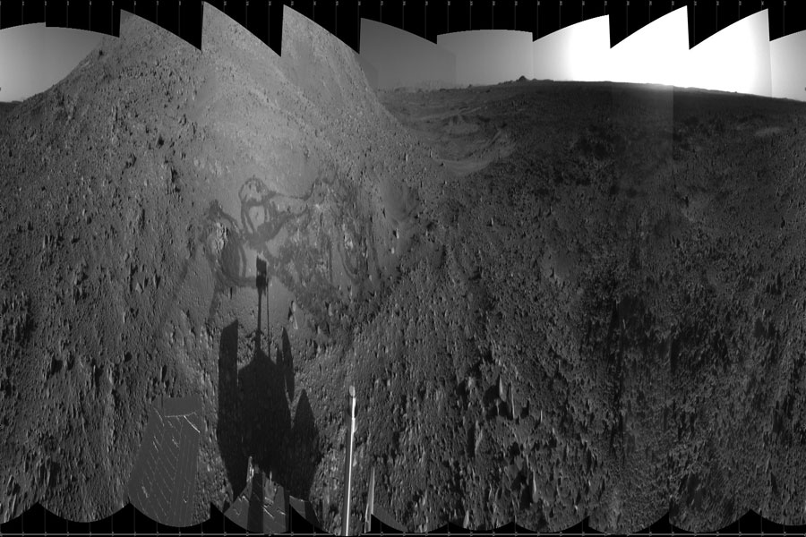 Das schwarzweiße Bild zeigt eine horizontal komprimierte Aussicht des Rovers Spirit auf dem Mars. Ein Klick auf das Bild zeigt ein breites Marspanorama.