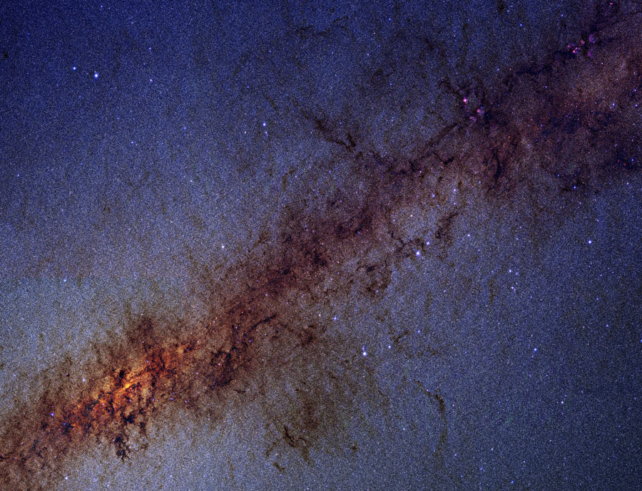 Von links unten nach rechts oben verläuft ein dunkelbraunes gefasertes Staubband vor einem Teppich aus Sternen.