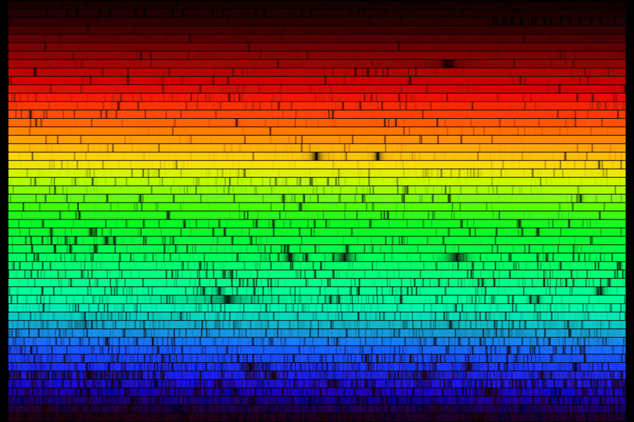 Das Bild zeigt ein Sonnenspektrum, das so lang ist, dass es in viele Zeilen aufgeteilt wurde. Oben ist ein breiter Bereich mit roten Zeilen, die nach einem schlalen orange und gelb gefärbten Zeilen in einen breiten grünen Bereich übergehen, unten folgt ein blauer Teil.