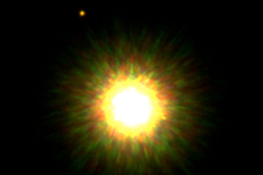 Ein heller weißer Fleck mit gelben Rand ist von einem Muster aus grünen und rötlichen Flecken umgeben. Links oben ist ein kleiner heller Lichtfleck.
