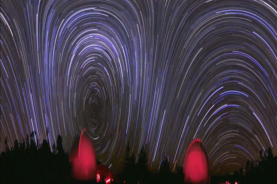 Hinter rot beleuchteten Sternwartekuppeln ragen Strichspuren von Sternen auf.