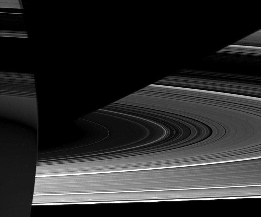 Links ist ein kleiner Teil von Saturn zu sehen, rechts daneben breiten sich die fragilen Ringe aus, die an eine Schallplatte erinnern.
