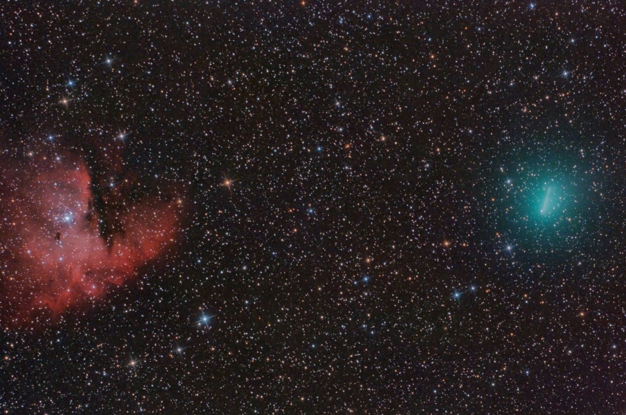 Hinter dicht verteilten Sternen leuchtet links ein roter Nebel, der an Pacman erinnert, und rechts einen türkisen Kometen, der eine Strichspur zieht, weil er schneller wandert als die Sterne.