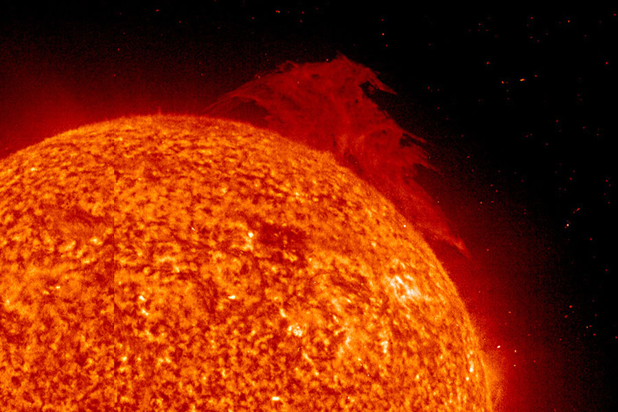Links unten ist die Sonne als orangefarbener Ball mit roten Strukturen dargestellt, rechts oben ist eine riesige dunkelrote Protuberanz.