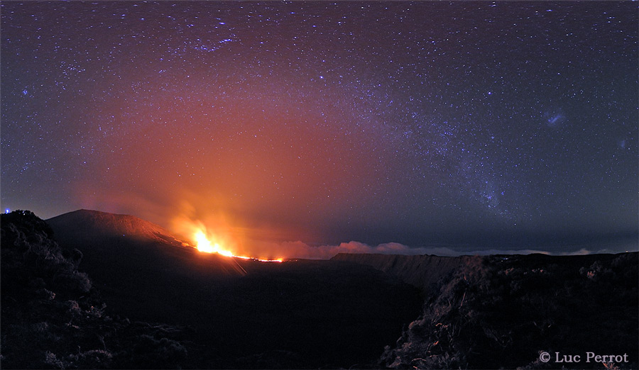 In der Dunkelheit leuchtet das Feuer eines aktiven Vulkans, darüber ist schwach die Milchstraße erkennbar.
