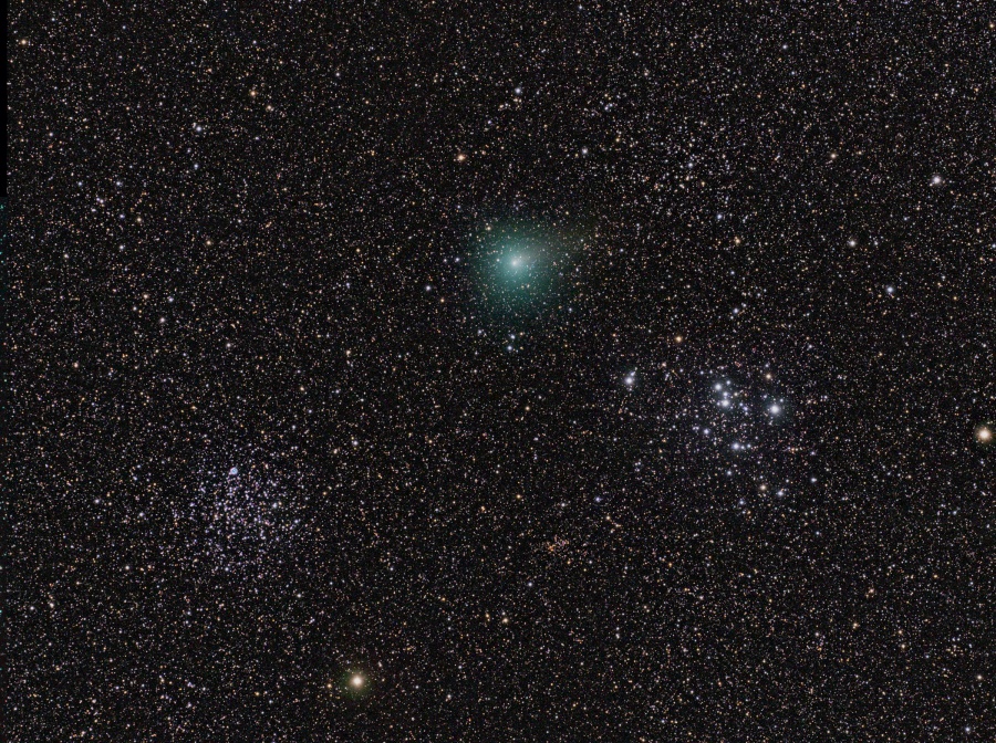 Vor einem sternengesprenkelten Hintergrund zeichnen sich zwei noch dichtere Sternhaufen ab, darüber leuchtet zwischen den beiden ein grünlicher Komet fast ohne Schweif.