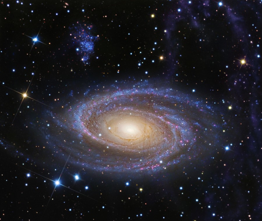 Umgeben von bunt gemischten Sternen schwebt die Spiralgalaxie M81 in der Bildmitte, sie hat besonders schön ausgeprägte bläuliche Spiralarme und einen hellgelben Kern.