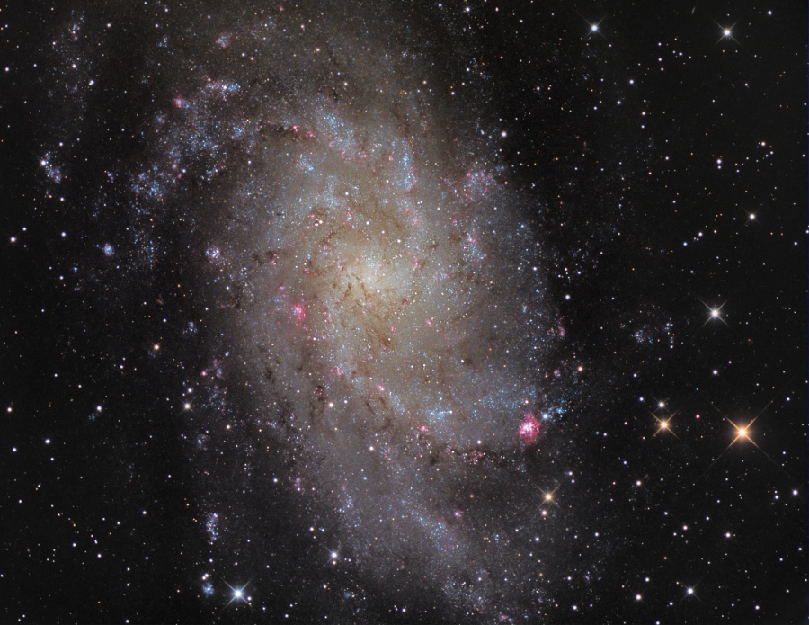 Mitten im Bild leuchtet eine flauschige Galaxie mit vielen Sternhaufen.
