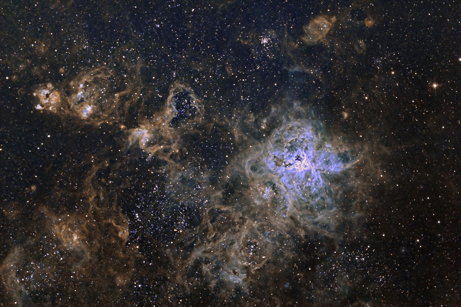Rechts neben der Mitte leuchten biolettblaue Nebelfasern in einem Gewirr von grau-braunen Nebelfasern, darüber sind zarte Sterne verstreuselt.