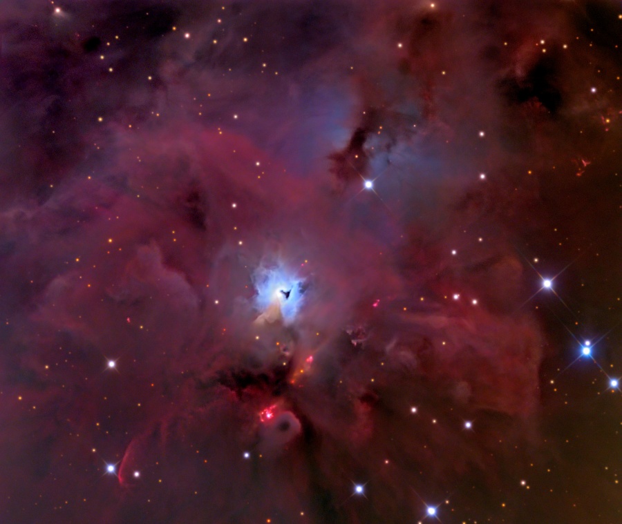 Bildfüllend sind dunkelrote Nebel hinter wenigen Sternen verteilt, in der Mitte ist ein hell leuchtender bläulicher Nebel mit einem schwarzen schlüssellochförmigen Nebel darin eingebettet.