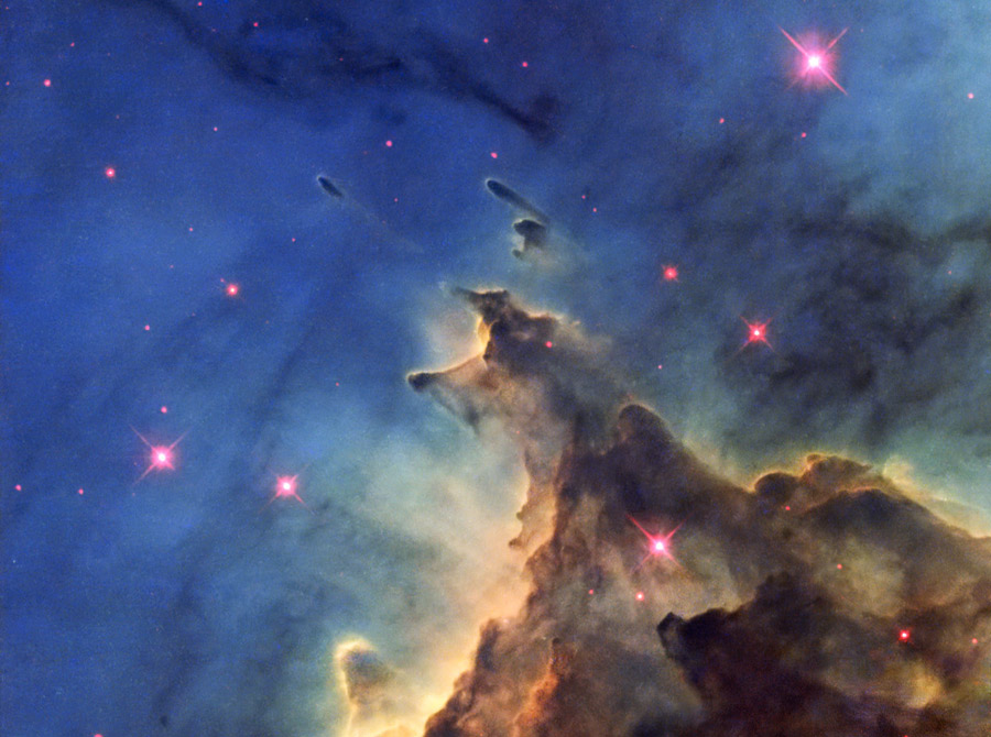 Vor einem leuchtenden Dunkelblau türmt sich rechts unten ein dunkelbrauner Nebel auf, der von hellen Rändern umgeben ist. Im Bild sind einige Sterne mit einem magentafarbenen Hof verteilt.