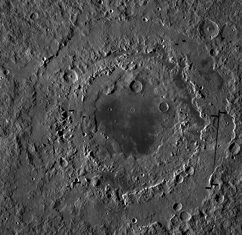 In der Bildmitte ist ein riesiger Krater mit mehreren Ringstrukturen, der von mehreren kleineren Kratern überlagert ist. In der Mitte ist eine dunkle Lavafläche.
