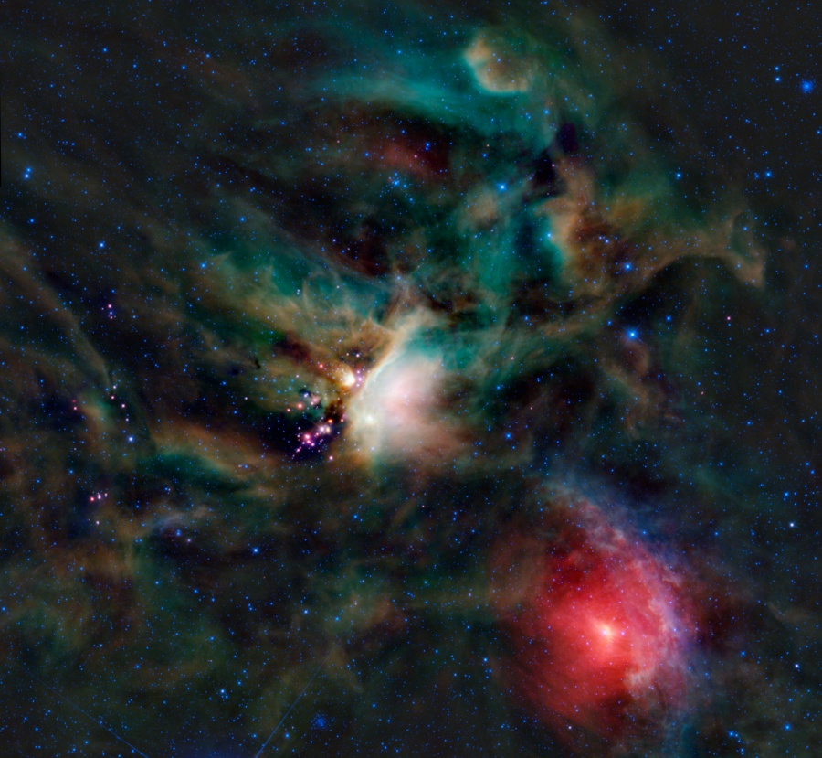 Mitten im Bild leuchten weißlich-grüne Staubnebel, die von dunklen Staubwolken umgeben sind. Rechts unten leuchtet ein heller roter Nebel um einen Stern.