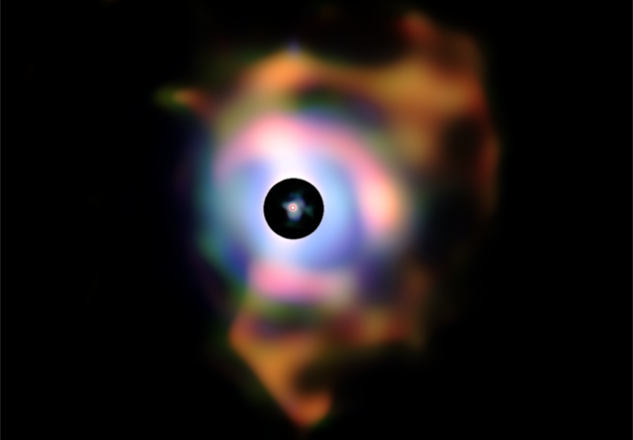 Auf schwarzem Grund leuchtet ein verschwommener Nebel aus bunten Flecken, in der Mitte befindet sich ein schwarzer Kreis, in dem wiederum ein verschwommener Nebel ist.