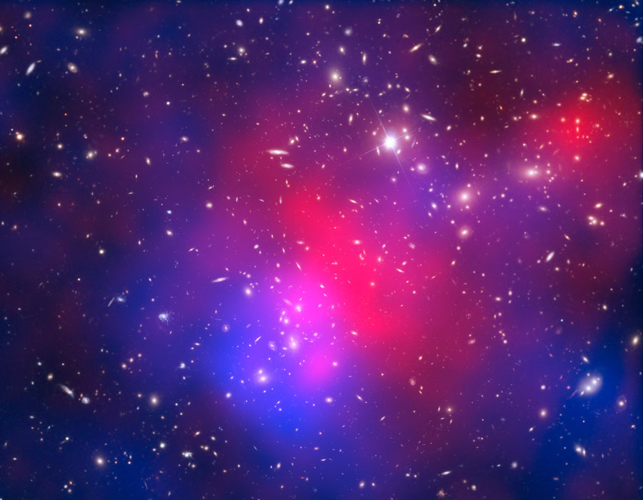 Das Bildfeld ist mit Galaxien gefüllt, in der Mitte leuchtet ein intensiv gefärbter Nebel, links unten blau, rechts oben rot, in der Mitte magentafarben.
