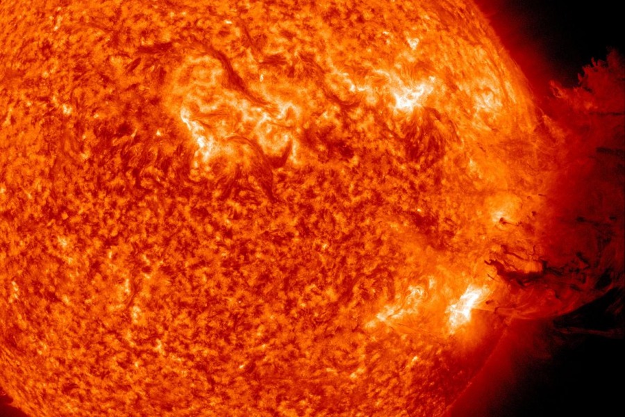 Die Sonne ist mit orangefarbenen Flecken überzogen. Nach rechts bricht eine Sonnenprotuberanz aus, die über den rechten Bildrand hinausreicht.