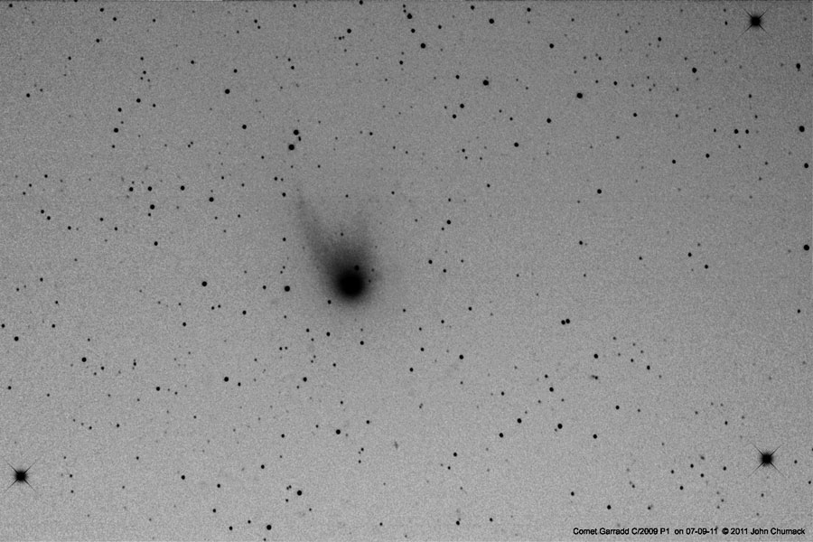 Auf dem grauen Bild sind Sterne und ein Komet mit Schweif schwarz abgebildet, es ist ein Negativbild.