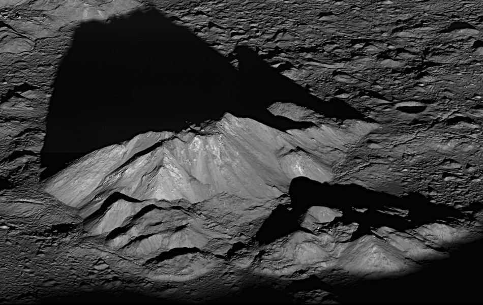 Mitten im Bild ragt ein Berg in einer felsigen Landschaft mit Kratern auf. Der Berg wirft einen langen Schatten.