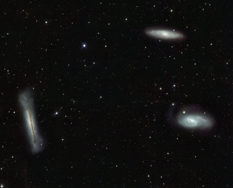 Im Bild sind drei Galaxien verteilt, rechts zwei spiralförmige, die man schräg von der Seite sieht, links eine flache Galaxie mit sehr breitem Wulst, die von der Kante sichtbar ist.