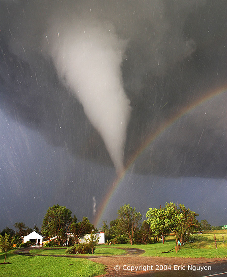 Vor einer dunklen Gewitterwolke leuchtet ein Regenbogen und ein heller Tornadowirbel. Vom Himmel fällt Hagel.