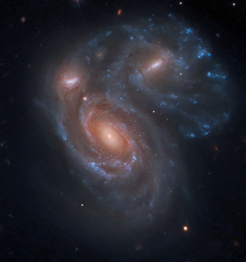 Im Bild sind mehrere Galaxienkerne, die von teils verzerrten, blau leuchtenden Spiralarmen umgeben sind.