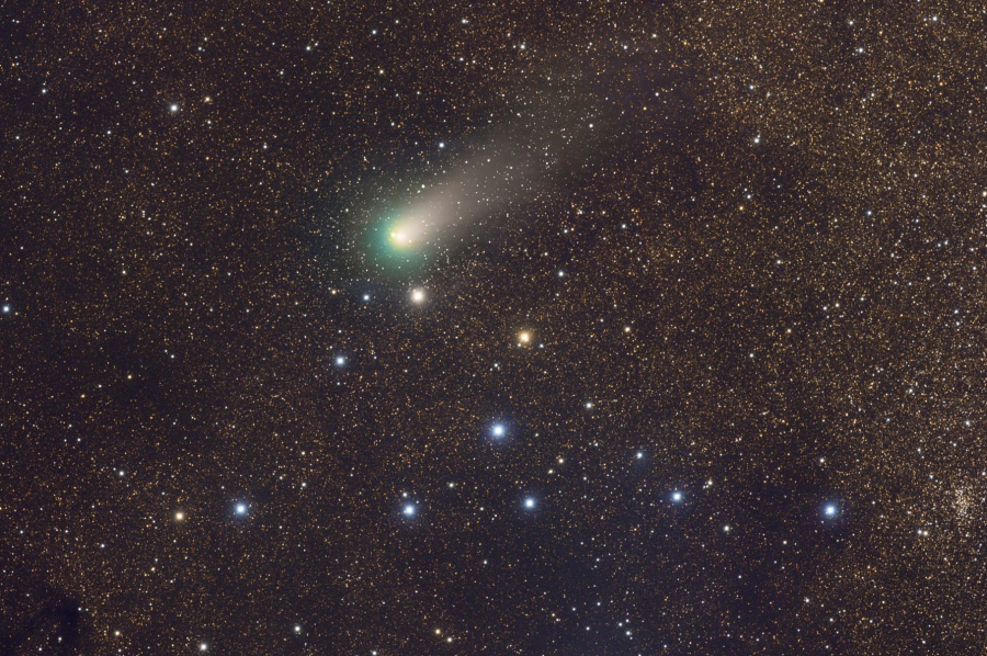Komet Garradd mit grüner Koma und einem kurzen Schweif nach links oben steht über einer Sterngruppe, die sich vom Hintergrund aus kleinen, schwachen Sternen abhebt.