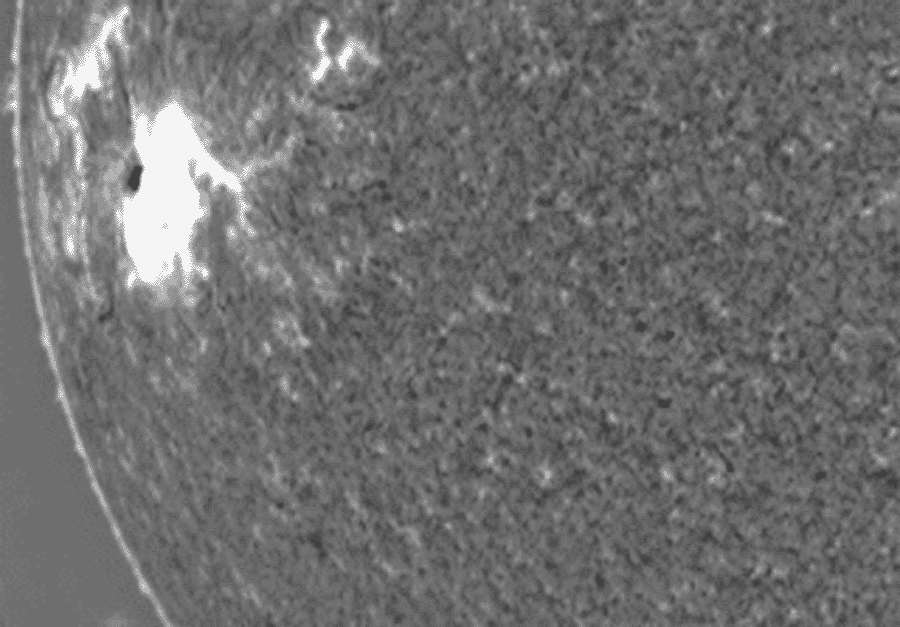 Der schwarzweiß dargestellte Ausschnitt der Sonne hat links am Sonnenrand einen sehr hellen Fleck, von dem sich eine Stoßwelle ausbreitet.