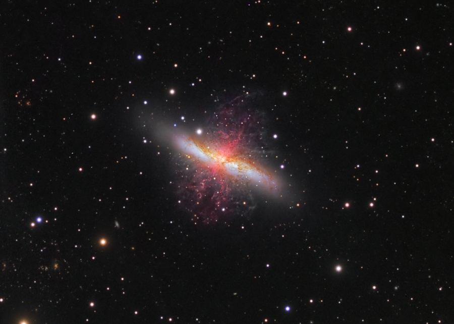 Mitten im Bild befindet sich die zerstört wirkende Zigarrengalaxie M82. Ihr heller Kern, der diagonal im Bild lieft, wird von roten Nebelfetzen gekreuzt.