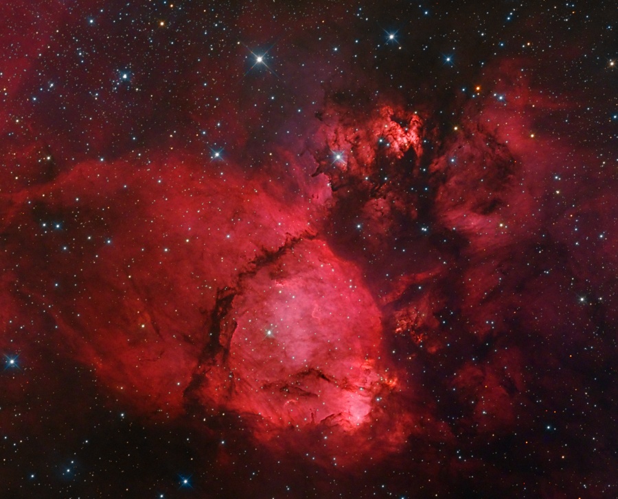 Ein leuchtend roter Nebel füllt das Bild, davor sind wenige kleine Sterne verteilt.