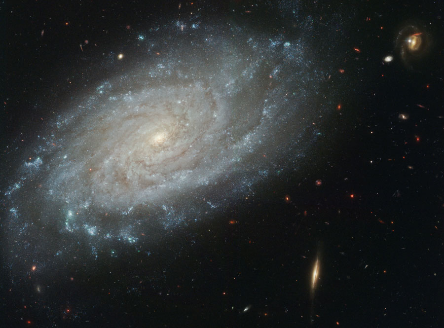 Bildfüllend ist eine Spiralgalaxie mit eng gewundenen dichten Spiralarmen abgebildet. Rechts darunter ist eine spindelförmige kleine Galaxie, die von der Seite sichtbar ist.