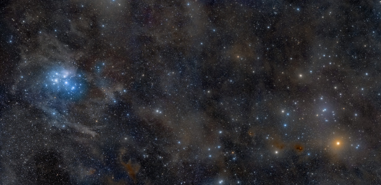 Links leuchten die Plejaden, sie sind von blauen Nebeln umgeben, rechts ein orangefarbener Stern, der ebenfalls von einem offenen Sternhaufen umgeben ist. Im Hintergrund sind braune Staubwolken und kleine Sterne verteilt.