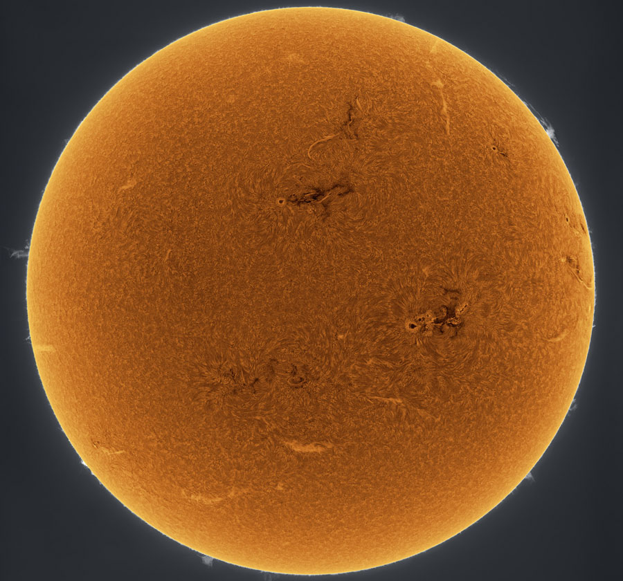 Der orangefarbene Ball auf dunklem Hintergrund ist die Sonne. Sie ist invertiert abgebildet, daher am Rand heller als in der Mitte. Auf der Oberfläche sind einige helle und dunkle Strukturen sowie Granulation.