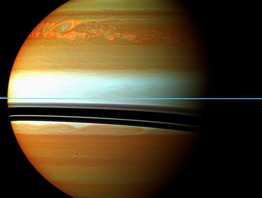 Bildfüllend ist der Körper des Planeten Saturn von der Seite zu sehen. Die Ringe sind ein schmaler blauer Strick, der quer durchs Bild verläuft. Waagrecht verlaufen Sturmzonen um den planeten, die farbverstärkt abgebildet sind. In der Mitte ist eine helle Zone, oben und unten sind orangefarbene Wolken. Oben ist ein riesiges Sturmgebiet. Die Schatten der Ringe fallen nach unten auf den Planeten.