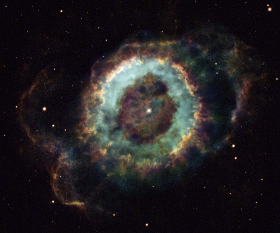 Der ringförmige Nebel im Bild erinnert an die Iris in einem Auge, innen grünblau mit einem ockerfarbenen Rand. In der Mitte der Pupille leuchtet ein Stern.