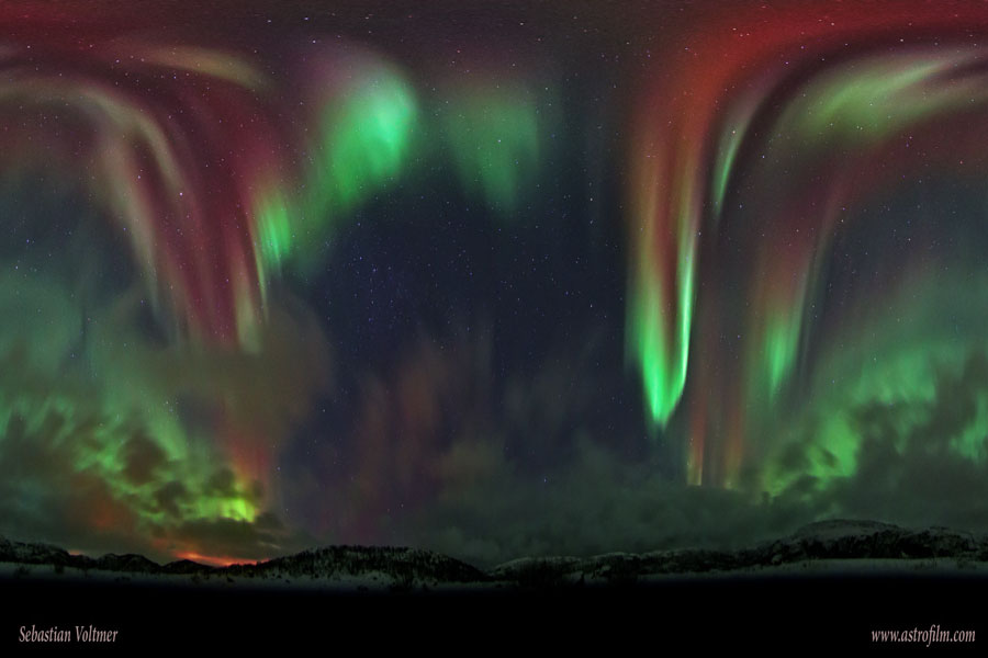 Am dunklen Himmel leuchtet ein riesiges grünes und rotes Polarlicht über Norwegen.