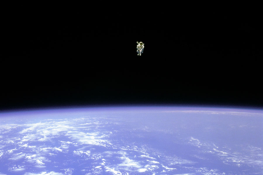 Über der Erde mit blauen Meeren und Wolken schwebt in weiter Ferne ein Astronaut im Raumanzug.