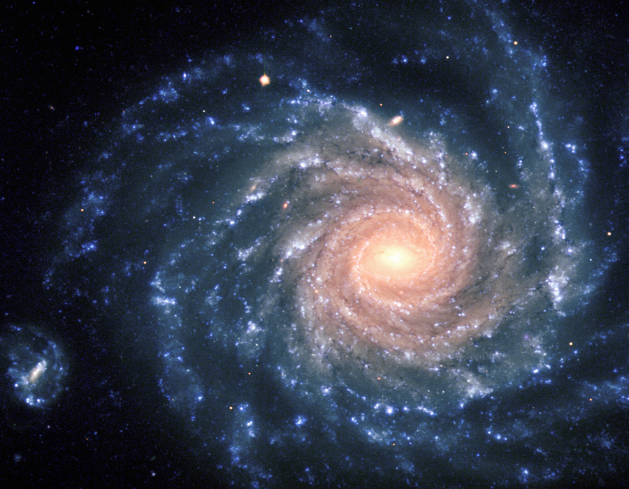 Im Bild ist die Spiralgalaxie NGC 1232 mit ausgeprägten Spiralarmen und Sternhaufen von oben zu sehen. Der Kern ist gelblich, nach außen hin wird die Galaxie orangefarben, die äußeren Spiralarme sind bläulich. Links unten im Bild ist eine kleine Galaxie mit Balken.
