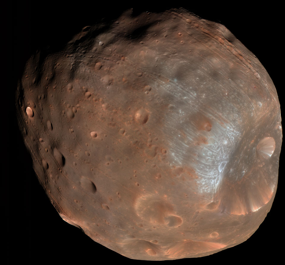 Der Himmelskörper im Bild erinnert an einen Asteroiden, er ist rötlich und vorne gräulich, auf seiner Oberfläche sind viele Krater, rechts ist ein besonders großer Krater, von dem ausgehend Rillen über den ganzen Körper verlaufen.