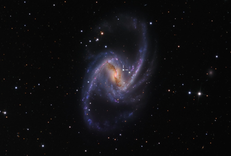 Das Bild zeigt eine verzerrte Galaxie mit einem breiten hellen Balken und zwei herausgezogenen Spiralarmen nach links unten und rechts oben. In der Mitte ist eine starke Staubbahn. Zwei Striche markieren eine Supernova.