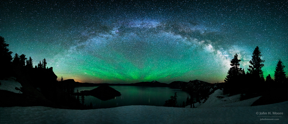 Über einem Kratersee wölbt sich die Milchstraße wie ein Bogen. Darunter leuchtet grünliches Nachthimmellicht. Am Himmel sind zahlreiche Sternbilder markiert, man sieht sie, wenn man den Mauspfeil über das Bild schiebt.