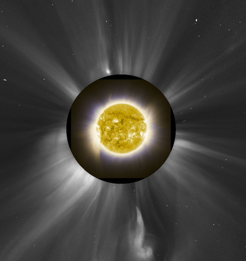 Mitten im Bild ist eine gelbe Kugel mit weißen und dunklen Strukturen, sie ist von weißen Schlieren umgeben, die in einen dunklen Kreis verlaufen. Außerhalb des dunklen Kreises sind lange Streifen und Strahlen der Sonnenkorona.